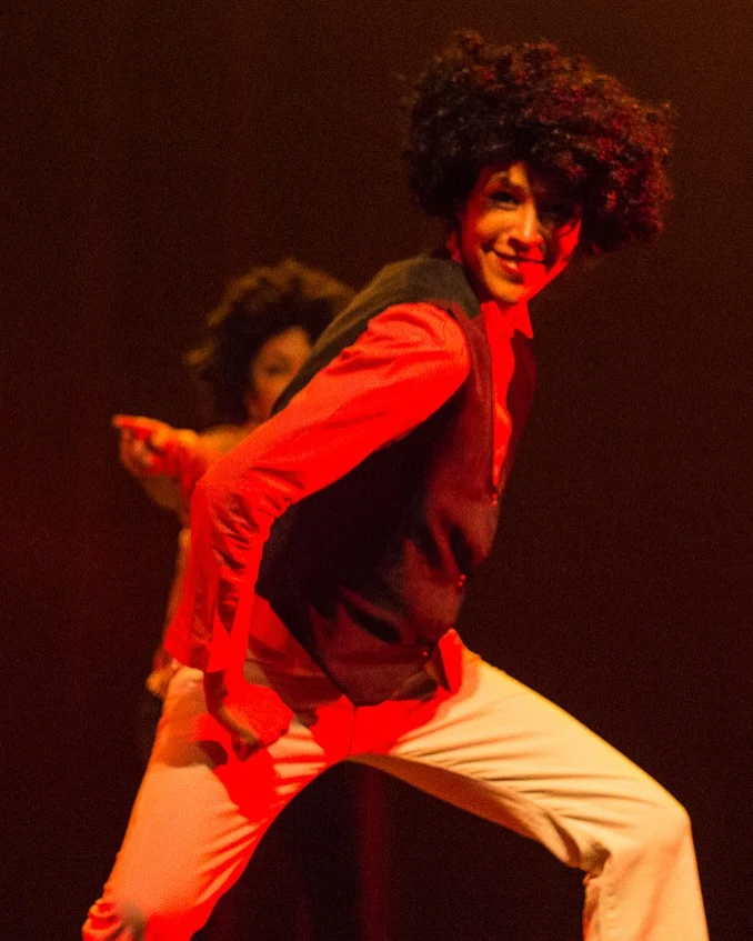 Bailarín con afro, camisa roja y chaleco en una interpretación de estética retro