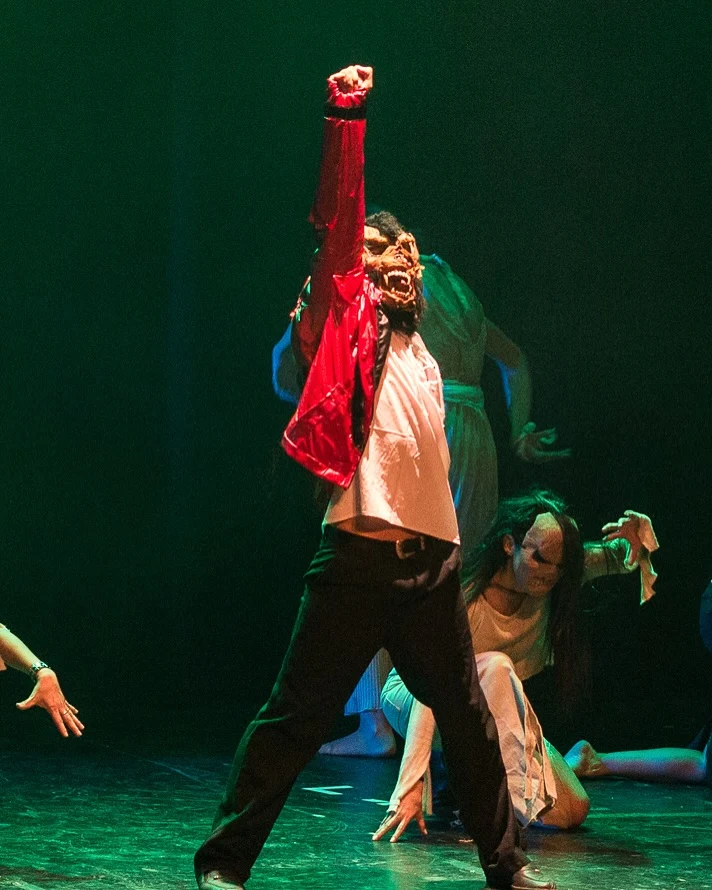 Intérprete con chaqueta roja y máscara levanta el brazo bajo luces verdes